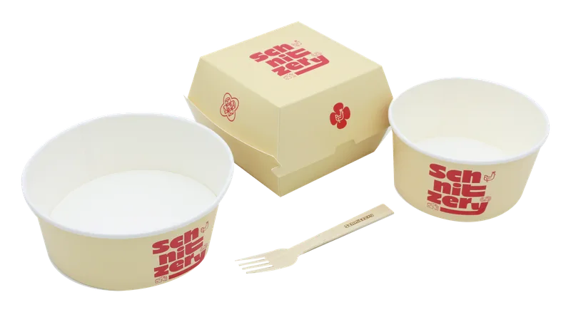 Verpackungsset von Schnitzery: cremefarbene Burgerbox, zwei Papier-Bowls mit rotem Logo und eine Holzgabel